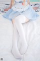 A woman in a blue dress and white stockings sitting on a bed.