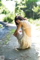 A woman in a white dress sitting on a dirt road.