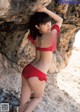 A woman in a red bikini leaning against a rock.