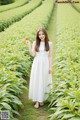 A woman in a white dress holding a flower in a field.