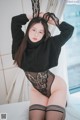 A woman in a black sweater and stockings posing on a bed.